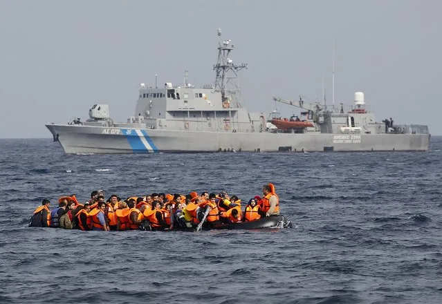 Syrian refugees call for help and empty water from their flooding raft as they approach  the Greek island of Lesbos past a Greek coast guard vessel October 20, 2015.Thousands of refugees – mostly fleeing war-torn Syria, Afghanistan and Iraq – attempt daily to cross the Aegean Sea from nearby Turkey, a short trip but a perilous one in the inflatable boats the migrants use, often in rough seas. (Photo by Yannis Behrakis/Reuters)