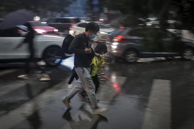 A man and a child wearing face masks to help curb the spread of the coronavirus walk across a street in the rain as motorists are clogged with heavy traffic on a road in Beijing, Wednesday, September 23, 2020. Xi Jinping, China's president and the leader of its Communist Party, cast the fight against the virus as an important exercise in international cooperation, an opportunity to “join hands and be prepared to meet even more global challenges”. (Photo by Andy Wong/AP Photo)