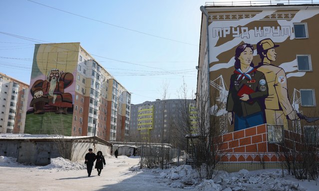 Locals walk past apartment buildings decorated with murals in Yakutsk on March 28, 2025. Yakutsk, six time zones east of Moscow, is the main city of the vast diamond-mining region of Yakutia which is one of the coldest inhabited regions on earth. (Photo by AFP Photo/Stringer)