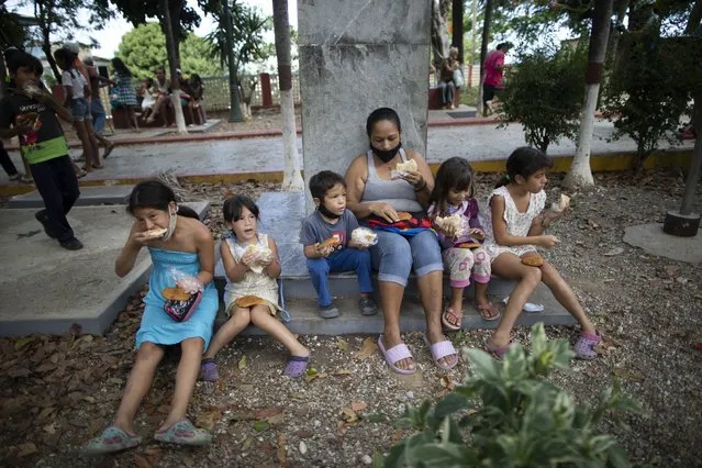 Children eat free arepas or corn flour patties, given to them by Andres Burgos, a 55-year-old publicist, in Macuto, Venezuela, Saturday October 24, 2020. Burgos, who is on a mission to feed the hungry, rode to the seaside city in Venezuela's La Guaira state, accompanied by other cyclists to distribute the arepas he made to needy children, adults and the elderly. (Photo by Ariana Cubillos/AP Photo)