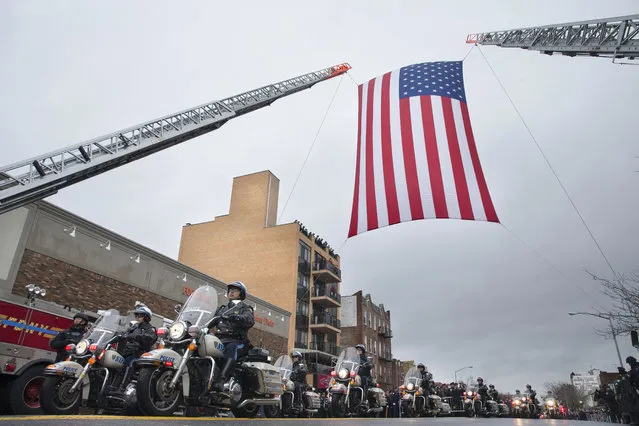 Motorcycle police officers ride under a giant American Flag as they lead the procession route during the funeral of New York Police Department Officer Wenjian Liu, Sunday, January 4, 2015, in the Brooklyn borough of New York. Liu and his partner, officer Rafael Ramos, were killed Dec. 20 as they sat in their patrol car on a Brooklyn street. The shooter, Ismaaiyl Brinsley, later killed himself. (Photo by John Minchillo/AP Photo)