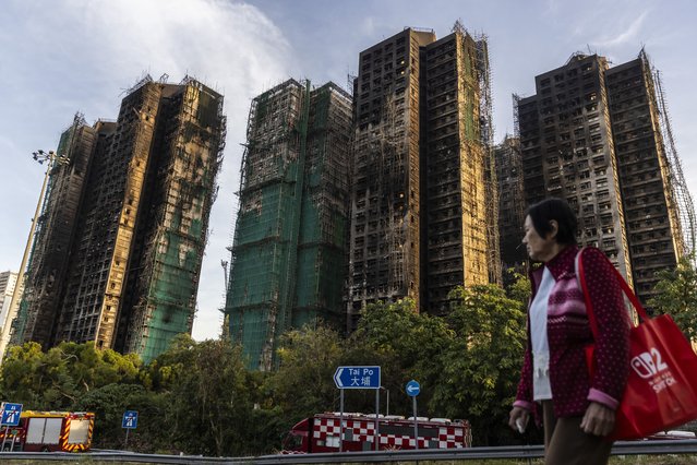 A woman walks past residential buildings damaged by fire at Wang Fuk Court in the Tai Po district on November 28, 2025 in Hong Kong, China. With at least 94 lives lost and rescue efforts ongoing, authorities allege gross negligence by contractors as firefighters work to fully extinguish remaining hotspots.Authorities have detained three individuals for questioning as investigators examine the cause of the blaze. (Photo by Isaac Lawrence/Getty Images)