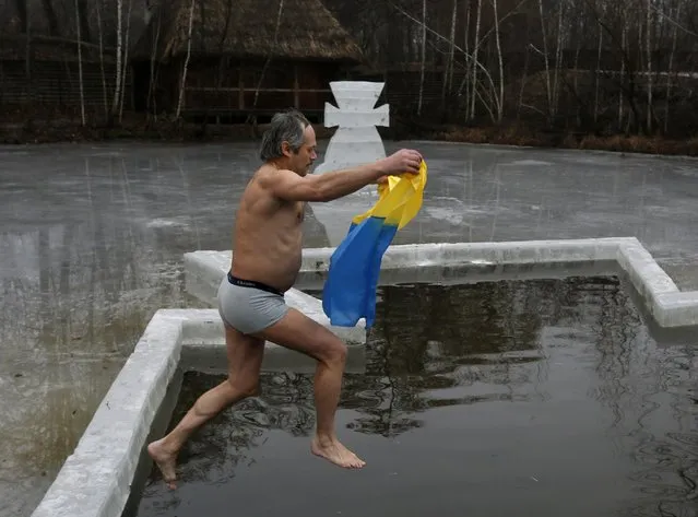 A man holding a Ukrainian flag while he jumps in the ice cold water during the celebration of the Epiphany in Kiev, Ukraine, Monday, January 19, 2015. (Photo by Sergei Chuzavkov/AP Photo)