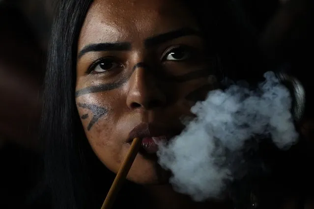 A Pataxo Indigenous woman smokes a traditional pipe during the Meeting of the First Peoples' ceremony at the 18th annual Free Land Indigenous Camp in Brasilia, Brazil, on April 8, 2022. (Photo by Eraldo Peres/AP Photo)