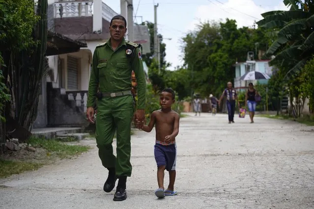 In this July 25, 2018 photo, a Cuban special brigade first lieutenant police officer walks with his son to a neighborhood party where they will cook a large stew, in Guantanamo, Cuba, near the U.S. naval base. It is tradition in Cuba for neighbors to pool their efforts to cook a large stew, using pork. (Photo by Ramon Espinosa/AP Photo)