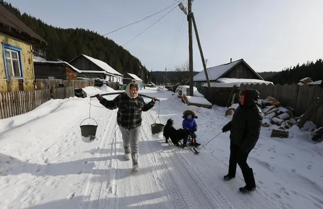 Oksana Shirshova, unemployed, talks to her neighbors as she carries a shoulder yoke with two buckets hanging on it after taking water from the Teryol river in Verkhnyaya Biryusa village, located in the Taiga area near the Russian Siberian city of Krasnoyarsk, February 16, 2015. (Photo by Ilya Naymushin/Reuters)