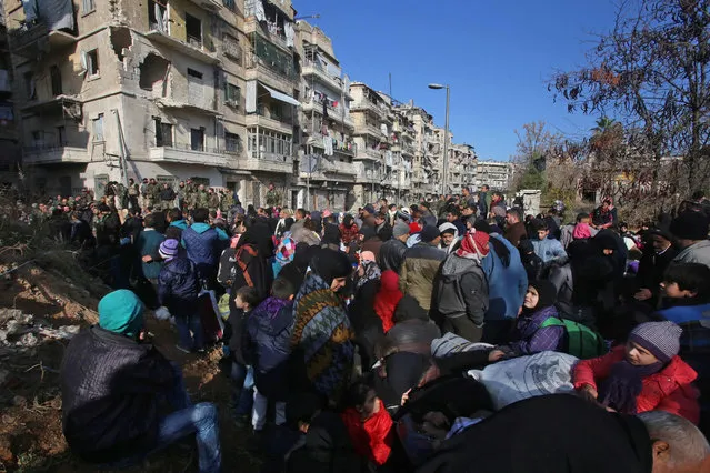 Syrian residents fleeing the violence gather at a checkpoint, manned by pro- government forces, in the Maysaloun neighbourhood of the northern embattled Syrian city of Aleppo on December 8, 2016. Syria' s army battled to take more ground from rebels in Aleppo after President Bashar al- Assad said victory for his troops in the city would be a turning point in the war. (Photo by Youssef Karwashan/AFP Photo)