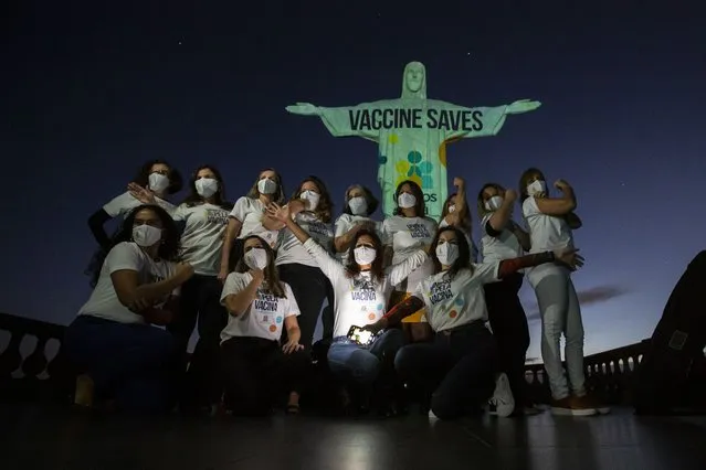 People pose in front of the Christ the Redeemer statue that is lit up with a message that reads in Portuguese; “Vaccination saves, united by the vaccine”, urging people to get the COVID-19 vaccine and encouraging vaccination in Brazil and throughout the world, in Rio de Janeiro, Brazil, Saturday, May 15, 2021. (Photo by Bruna Prado/AP Photo)