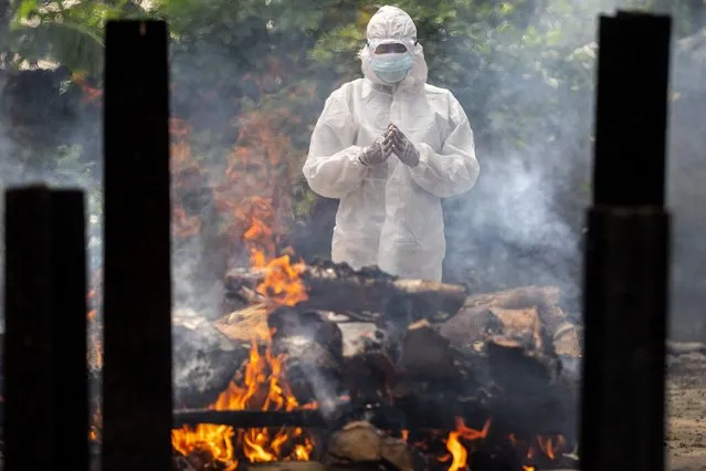 A relative in protective suit performs last rituals near the body of a person who died of COVID-19 during cremation in Gauhati, India, Monday, May 24, 2021. India crossed another grim milestone Monday of more than 300,000 people lost to the coronavirus as a devastating surge of infections appeared to be easing in big cities but was swamping the poorer countryside. (Photo by Anupam Nath/AP Photo)