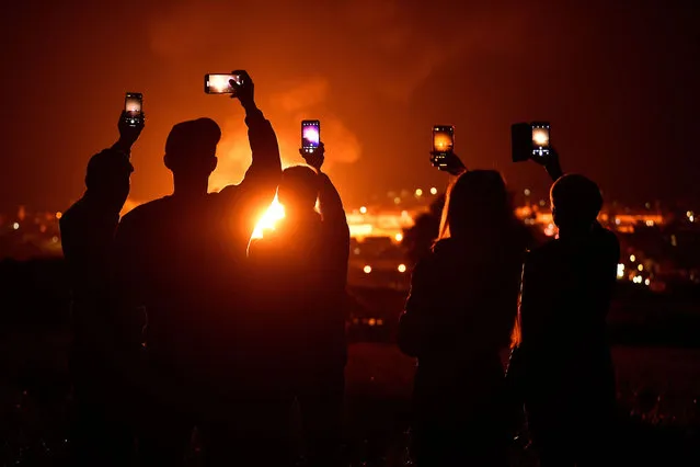 People pose holding their phones to take pictures of the completed Craigyhill bonfire while it burns standing at 202.37208 ft, measured by an independent land survey company, aiming to break the world record of tallest bonfire, on the “eleventh night” in order to usher in the Twelfth of July celebrations, held by unionists, in Larne, Northern Ireland July 11, 2022. Loyalists are lighting bonfires across Northern Ireland as part of a tradition to mark the anniversary of Protestant King William's victory over the Catholic King James at the Battle of the Boyne in 1690. (Photo by Clodagh Kilcoyne/Reuters)