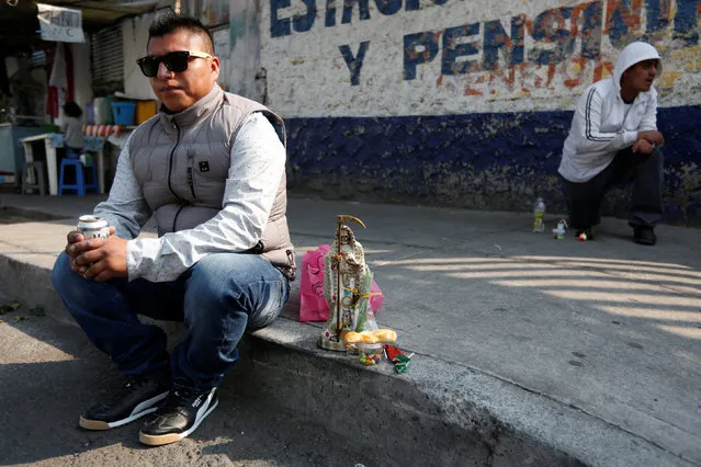 A man sits next to a figurine of Santa Muerte or The Saint of Death during the first prayer of the New Year in Mexico City, Mexico January 1, 2017. (Photo by Carlos Jasso/Reuters)