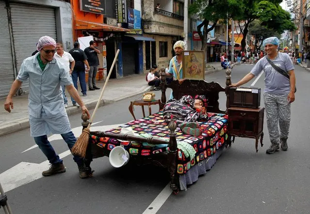 Men push a bed with a woman sleeping on it during the celebration of the World Day of Laziness in Itagui, Colombia, on August 21, 2022. (Photo by Fredy Builes/AFP Photo)