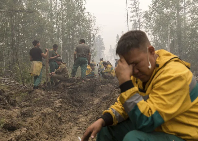 Employees of the Yakutlesresurs rest as they dig a firebreak moat to stop a forest fire outside Magaras village 87 km. (61 miles) west of Yakustk, the capital of the republic of Sakha also known as Yakutia, Russia Far East, Sunday, July 18, 2021. Russia has been plagued by widespread forest fires, blamed on unusually high temperatures and the neglect of fire safety rules, with the Sakha-Yakutia region in northeastern Siberia being the worst affected. (Photo by Alexey Vasilyev/AP Photo)