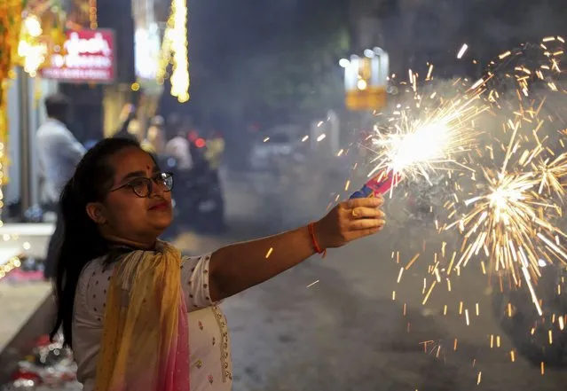 A girl lights firecrackers as she celebrates Diwali, the festival of lights, in Hyderabad, India, Thursday, Noember. 4, 2021. Hindus light lamps, wear new clothes, exchange sweets and gifts and pray to goddess Lakshmi during Diwali, the festival of lights. (Photo by Mahesh Kumar A./AP Photo)