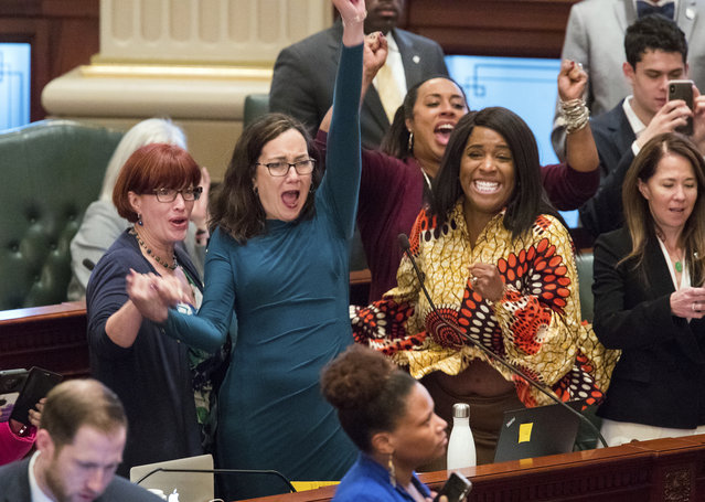 Illinois state Rep. Kelly Cassidy, D-Chicago, throws her fist in the air as she celebrates with Illinois state Senator Heather Steans, D-Chicago, left, and Rep. Jehan Gordon-Booth, D-Peoria, as they watch the final votes come in for their bill to legalize recreational marijuana use in the Illinois House chambers Friday, May 31, 2019. The 66-47 vote sends the bill to Gov. J.B. Pritzker who indicated he will sign it. (Photo by Ted Schurter/The State Journal-Register via AP Photo)