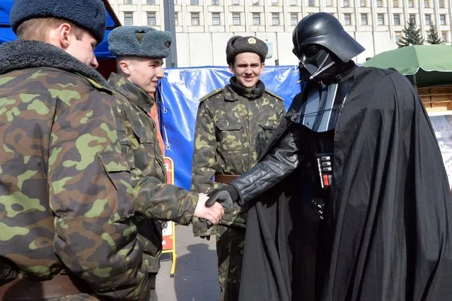 A man wearing the outfit of iconic movie villain Darth Vader (R), who announced he was running for president as the official candidate of the Ukrainian Internet Party (UIP), meets with Ukrainian soldiers within a protest action in front of the Central Election Commission building in Kiev on April 3, 2014.(Photo by Sergei Supinsky/AFP Photo)