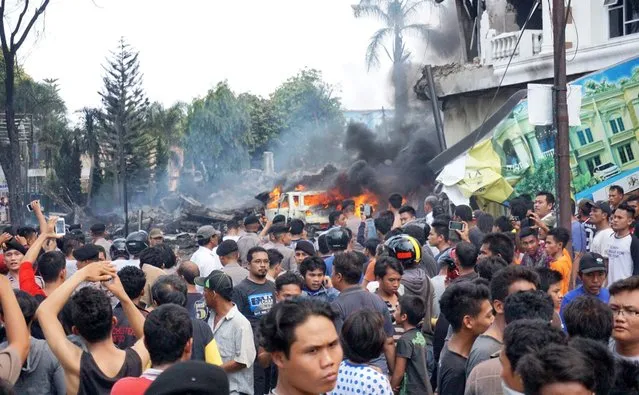Residents gather next to the crash site of a military Hercules plane in Medan, North Sumatra province on June 30, 2015. An Indonesian military transport plane crashed shortly after take off in the city, an official said, with the plane exploding in a ball of flames. (Photo by Muhammad Zulfan Dalimunthe/AFP Photo)