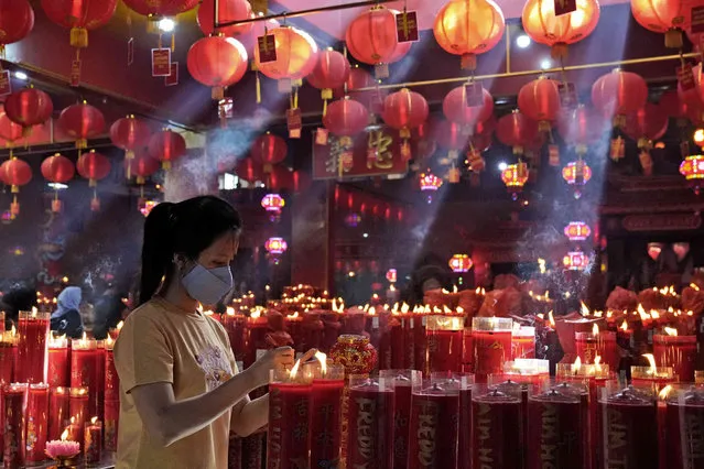 A woman lights a candle during the lunar New Year celebrations at the Hok Lay Kiong temple in Bekasi, Indonesia, Tuesday, February 1, 2022. The celebration marks the Year of the Tiger in the Chinese Zodiac calendar. (Photo by Dita Alangkara/AP Photo)