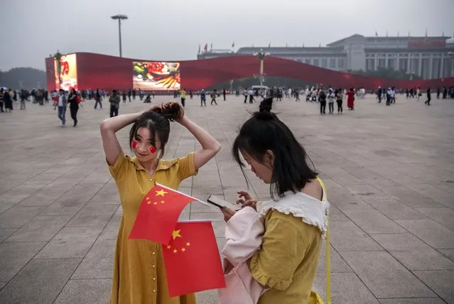 A Chinese woman adjusts her hair as a friend holds the national flag as they visit Tiananmen Square on September 27, 2019 in Beijing, China. China will mark the 70th anniversary of the founding of the People's Republic of China in 1949 on October 1st. (Photo by Kevin Frayer/Getty Images)