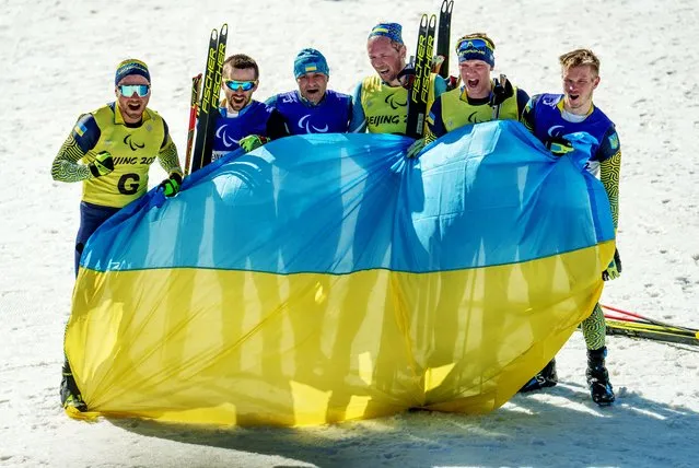 Ukrainian paralympic athletes, bronze medallist Anatolii Kovalevskyi, with guide Oleksandr Mukshyn, gold medallist Vitalii Lukianenko, with guide Borys Babar, and silver medallist Dmytro Suiarko, with guide Oleksandr Nikonovych celebrate with their country's flag after competing at the Beijing 2022 Winter Paralympic Games Para Biathlon, Men's Middle Distance Vision-Impaired event at National Biathlon Centre in Zhangjiakou, China on March 8, 2022. (Photo by Thomas Lovelock/OIS/Handout via Reuters)