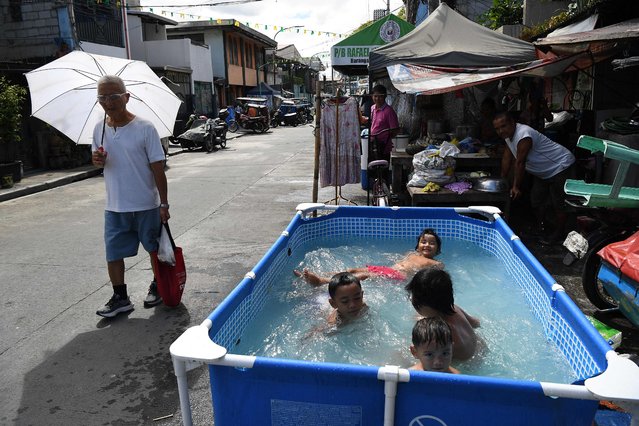 A pedestrian holding an umbrella walks past children cooling off on a makeshift pool along a street in Manila on May 3, 2024, amidst a heat wave. (Photo by Ted Aljibe/AFP Photo)