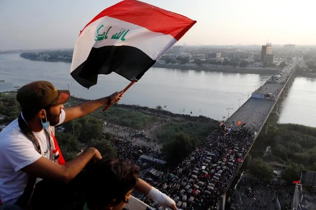 A demonstrator holds an Iraqi flag as he sits on a building during an anti-government protests in Baghdad, Iraq October 30, 2019. (Photo by Thaier Al-Sudani/Reuters)