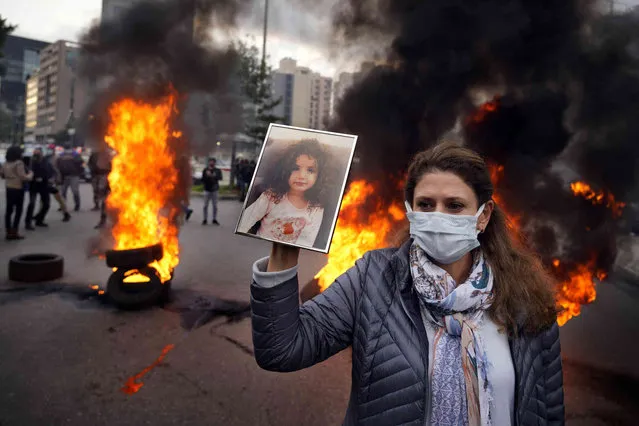 A woman holds a picture of her granddaughter, who was killed in the deadly 2020 Beirut port explosion, as others burn tires to block a road during a demonstration outside the Justice Palace in support of the judge investigating the blast after he was forced to suspend his work, in Beirut, Lebanon, Monday, February 7, 2022. (Photo by Bilal Hussein/AP Photo)