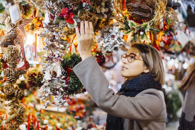 Young woman choosing Christmas decoration on a Christmas Market in Barcelona, Spain. (Photo by Alexander Spatari/Getty Images)