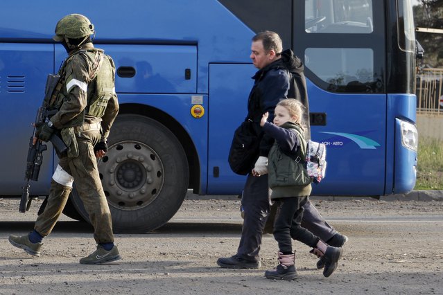 A man and a girl who left a shelter in the Metallurgical Combine Azovstal walk to a bus escorting by a serviceman of Russian Army in Mariupol, in territory under the government of the Donetsk People's Republic, eastern Ukraine, Friday, May 6, 2022. (Photo by Alexei Alexandrov/AP Photo)