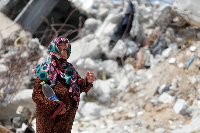 A Palestinian woman, whose house was destroyed by what witnesses said was Israeli shelling during a 50-day war last summer, holds a bottle as she walks outside her makeshift shelter during a wave of heat in Khan Younis in the southern Gaza Strip August 3, 2015. (Photo by Ibraheem Abu Mustafa/Reuters)