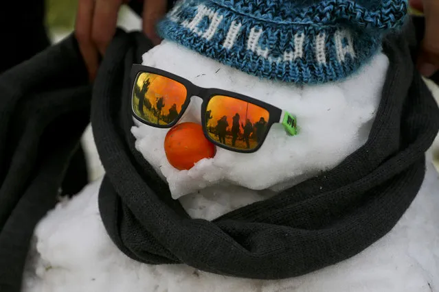 A man wraps a scarf on a snowman decked out with sunglasses, a knitted cap and an orange serving as a nose, as others play in a snow-covered park in Santiago, Chile, Saturday, July 15, 2017. Record cold temperatures and an unusual snowfall hit Chile's capital Saturday. Normal temperatures are expected to return midweek. (Photo by Esteban Felix/AP Photo)