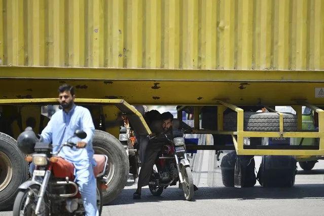 Commuters try to make their along a road partially blocked with transport trucks placed by local authorities in Rawalpindi on May 25, 2022, as all roads leading into Pakistan's capital were blocked ahead of a major protest planned by ousted prime minister Imran Khan and his supporters. (Photo by Farooq Naeem/AFP Photo)