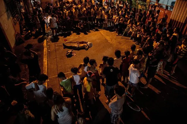 This file photo taken on August 2, 2017 shows residents looking at the body of an alleged drug user killed by unidentified assailants in Manila. Philippine police killed 32 people in “shock and awe” raids aimed at scaring drug traffickers, authorities said on August 16, after President Rodrigo Duterte admitted to setbacks in his controversial crime war. (Photo by Noel Celis/AFP Photo)