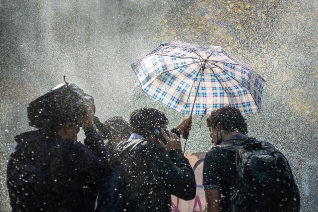 A group of students hide behind an umbrella, to repel the water thrown by the police cars on April 28, 2022 in Santiago de Chile. Amid at demonstration of secondary students from public education, demanding at the government, improvements in the infrastructure of educational establishments, more teachers, decent food, as well as the creation of a protocol for the integration of LGBTQ+ communities, among other demands. (Photo by Claudio Abarca Sandoval/NurPhoto via Getty Images)