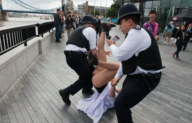 British policemen block a topless activist of Ukraine's prominent feminist rights group FEMEN as she was protesting near the Tower Bridge in Central London on August 2, 2012 on day 6 of the London 2012 Olympic games. FEMEN's activists organised an “islamic maraton” to demonstrate against “islamic regimes” they say being supported by the International Olympic Committee. (Photo by Will Oliver/AP Photo)