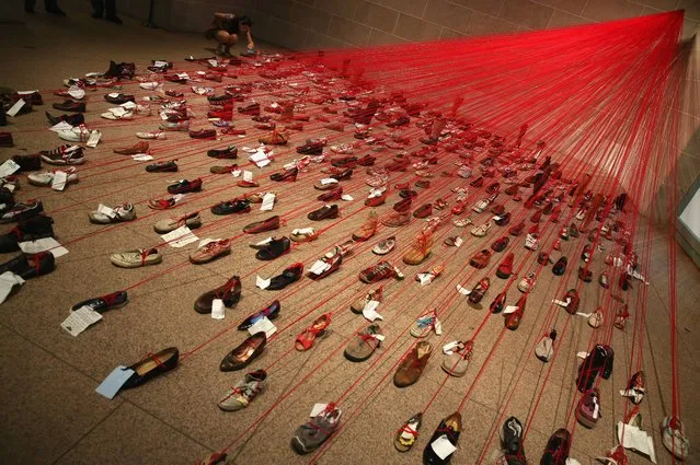 Visitors examine the art exhibit called  “Perspectives” that is on display at the Smithsonian's Arthur M. Sackler Gallery, August 21, 2014 in Washington, DC. Perspectives transforms over 400 shoes attached to red yarn and handwritten notes into a dramatic and emotionally charged installation. (Photo by Mark Wilson/Getty Images)