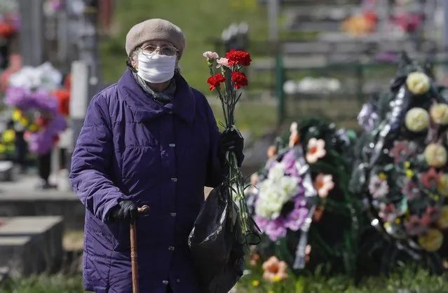 An elderly woman wearing a face mask to protect from coronavirus stands next the grave of her relative, during a traditional Orthodox Christian ceremony, in the town of Novogrudok, 150 km (93 miles) west of Minsk, Belarus, Tuesday, April 28, 2020. Tuesday marked celebrations of the church holiday "Radunitsa", a day of remembrance for the dead, on the ninth day after Orthodox Easter. Some people wear face masks to protect against COVID-19, although Belarus' president has dismissed concerns about the coronavirus despite a sharp rise in infections. (Photo by Sergei Grits/AP Photo)