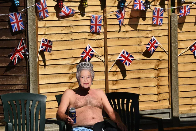 Terry Livesey wearing a mask of Britain's Queen Elizabeth II, sunbathes in his garden surrounded by Union flags as people mark the 75th anniversary of VE Day (Victory in Europe Day), the end of the Second World War in Europe in Portslade, southern England on May 8, 2020. (Photo by Glyn Kirk/AFP Photo)