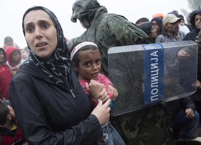A woman holds a girl as she passes the border from the northern Greek village of Idomeni to southern Macedonia, Thursday, September 10, 2015. Thousands of people, including many families with young children, braved torrential downpours to cross Greece's northern border with Macedonia early Thursday, after Greek authorities managed to register about 17,000 people on the island of Lesbos in the space of a few days, allowing them to continue their journey north into Europe. (Photo by Giannis Papanikos/AP Photo)