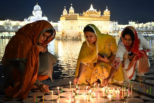 Devotees light candles while paying respect at the illuminated Golden Temple on the occasion of the Bandi Chhor Divas, a Sikh festival coinciding with Diwali, the Hindu festival of lights, in Amritsar on October 24, 2022. (Photo by Narinder Nanu/AFP Photo)