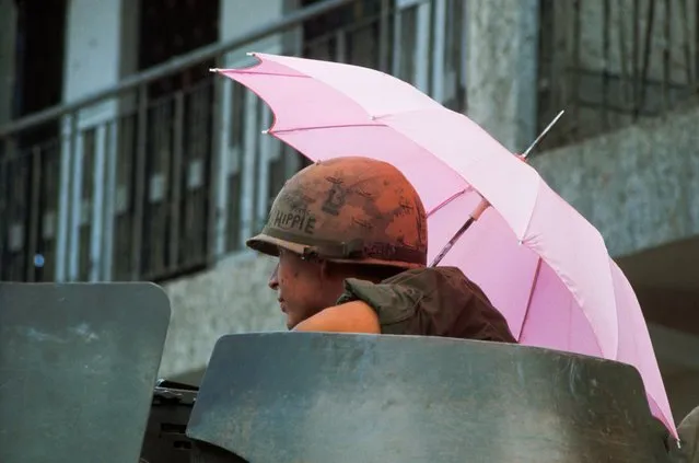 A US soldier from 8ieme Regiment, riding atop a 9th Division armored personnsl carrier, shelters beneath a pink umbrella at Saigon, during the mini-Tet offensive. Vietnam, 1968. (Photo by Tim Page/Corbis via Getty Images)