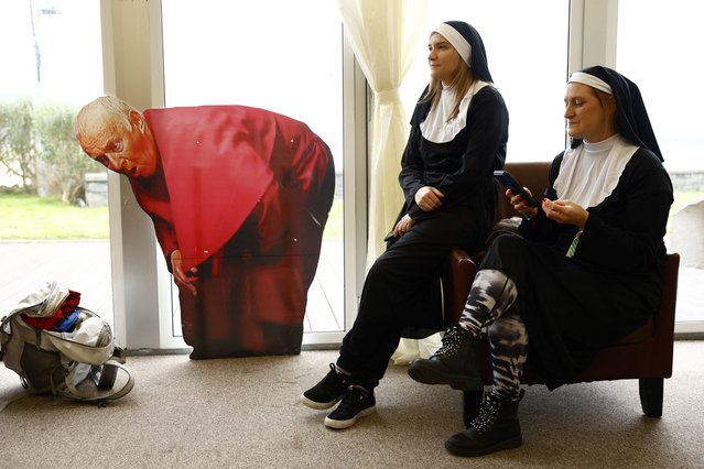 People in costumes sit next to a cardboard cutout picture of the character of “Bishop Brennan” as they attend the Friends of Ted Festival, or TedFest, an annual fan convention held on the largest of the Aran islands, for fans of the sitcom Father Ted, in Inis Mor, Ireland on March 9, 2024. (Photo by Clodagh Kilcoyne/Reuters)