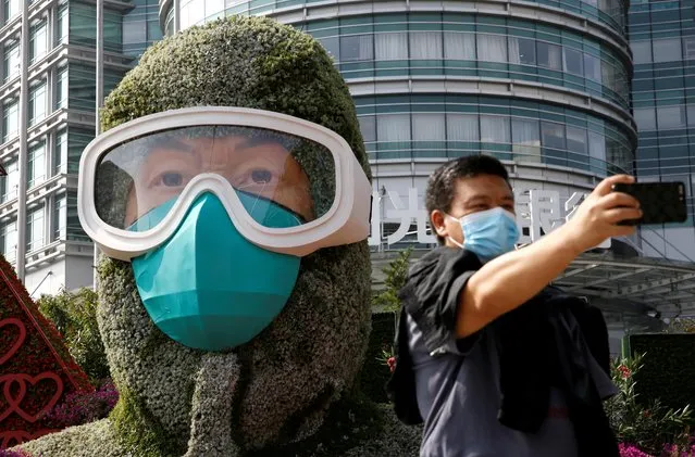 A man wearing a face mask takes selfies in front of a floral installation featuring a medical worker in the fight against the coronavirus disease (COVID-19), set up ahead of Chinese National Day on October 1, on Changan Avenue in Beijing, China on September 25, 2020. (Photo by Tingshu Wang/Reuters)