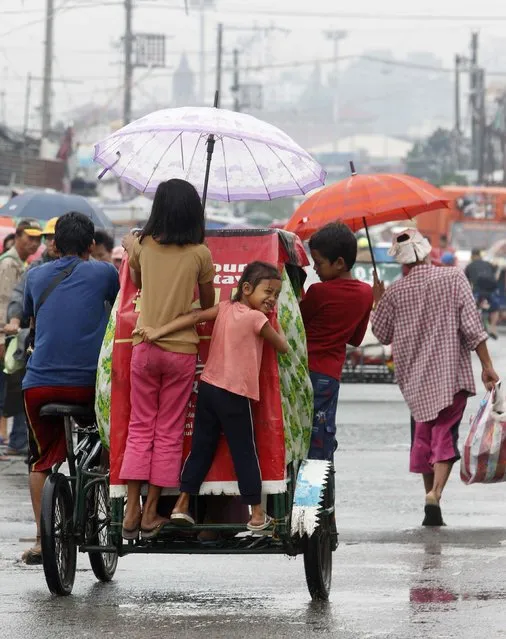 A girl smiles as she holds on to a pedicab, as her family goes back to their house after taking shelter at an evacuation center during typhoon Hagupit, in Manila December 9, 2014. (Photo by Cheryl Gagalac/Reuters)