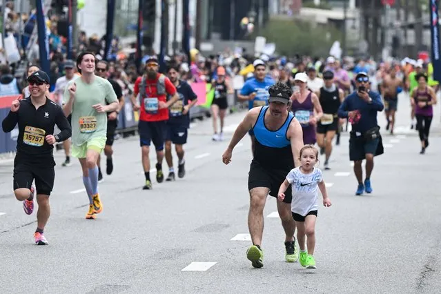 A runner and child run to cross the finish line during the 38th Los Angeles Marathon in Los Angeles, California, on March 19, 2023. (Photo by Patrick T. Fallon/AFP Photo)