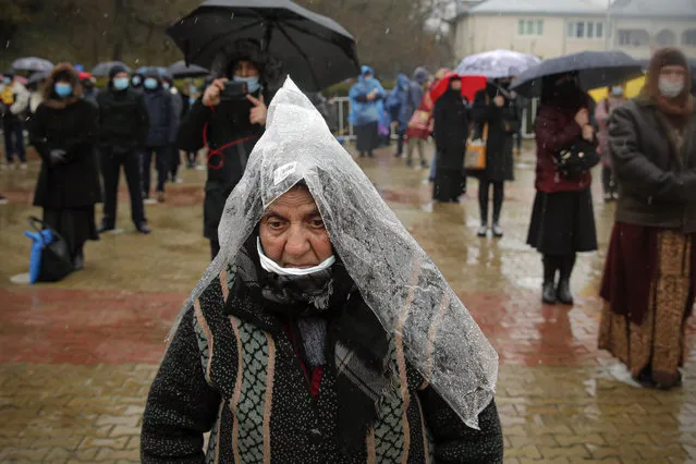 A woman using a plastic sheet as rain protection attends a religious service celebrating St. Andrew in the village of Ion Corvin, eastern Romania, Monday, November 30, 2020. Braving wintry weather and the new coronavirus fears, several hundred Orthodox Christian believers gathered outside a cave in eastern Romania where St. Andrew is said to have lived and preached in the 1st century. (Photo by Vadim Ghirda/AP Photo)