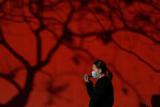 A woman wearing a face mask to help curb the spread of the coronavirus talks on her smartphone as she walks by tree shadow cast on a truck parked on a street in Beijing, Monday, December 7, 2020. (Photo by Andy Wong/AP Photo)