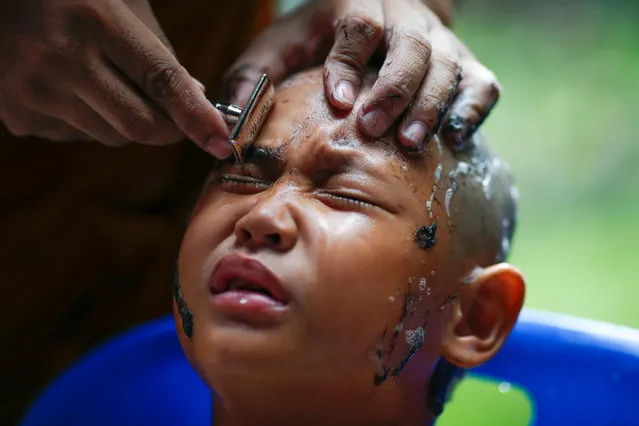 A young Thai boy reacts as he has his eyebrows shaved by Buddhist monk during a mass ordination to honor the late Thai King Bhumibol Adulyadej at a temple in Bangkok, Thailand, 20 October 2016. A total of 108 Thai men and 48 of youngsters are to be ordained as monks and novices to honor the late Thai king as part of the nation mourning. King Bhumibol, the world's longest reigning monarch died at the age of 88 in Siriraj hospital on 13 October 2016. (Photo by Rungroj Yongrit/EPA)