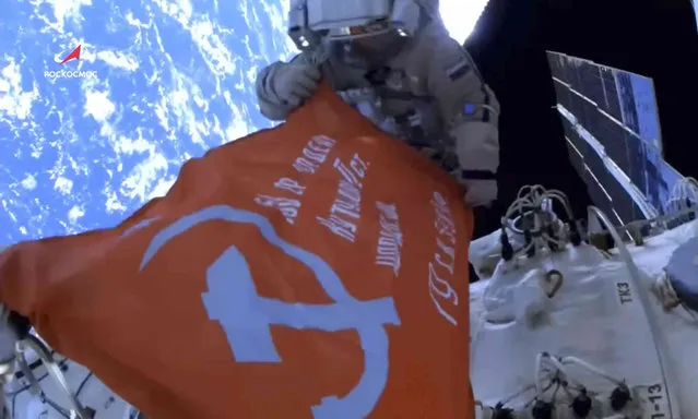 In this photo taken from video footage released by Roscosmos Space Agency, Roscosmos' cosmonauts Oleg Artemyev and Denis Matveev unfold a copy of the Soviet Victory Banner in World War II during their spacewalk on the International Space Station (ISS), Thursday, April 28, 2022. (Photo by Roscosmos Space Agency via AP Photo)