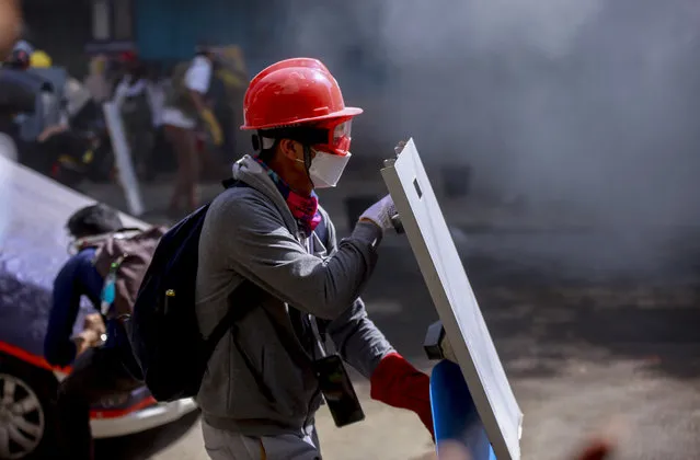 An anti-coup protester with a makeshift shield braves teargas during a demonstration in Yangon, Myanmar Thursday, March 4, 2021. (Photo by AP Photo/Stringer)